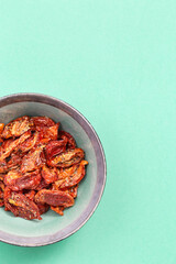 Sun dried tomatoes slices with Italian herbs and spices on mint colored ceramic plate. Homemade dehydrated vegetable.