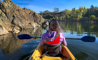 Back view middle age woman holding paddle in double kayak looking at beautiful river view 