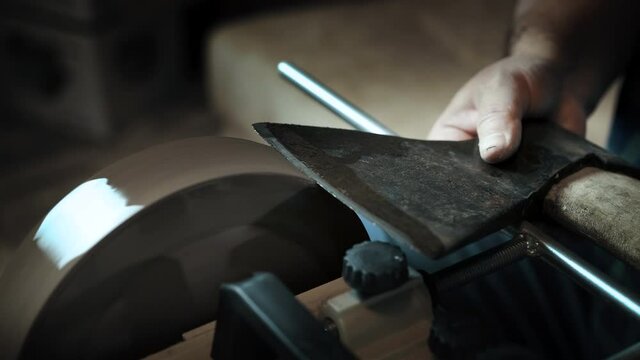 Asian man sharpening axe on a grinder
