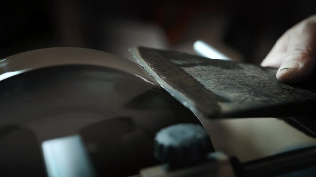 Asian man sharpening axe on a grinder. Macro shoot