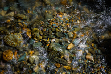 Rocky bottom of mountain river through the clear water, selective focus, blurring the image. Cristal water in the stream shimmers in sunlight. Stone background.