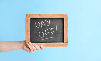 Female hand holding chalkboard with text DAY OFF on color background