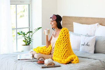 Morning of beautiful young woman with warm plaid having breakfast in bed
