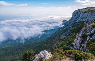 A majestic view of the rocky mountains and the valley in fog and clouds. Creamy fog covered the mountain valley in sunset light. Picturesque and gorgeous scene. Misty sunset over Crimea Mountains