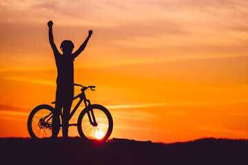 Fototapeta premium Silhouette of a mountain biker at sunset with arms raised