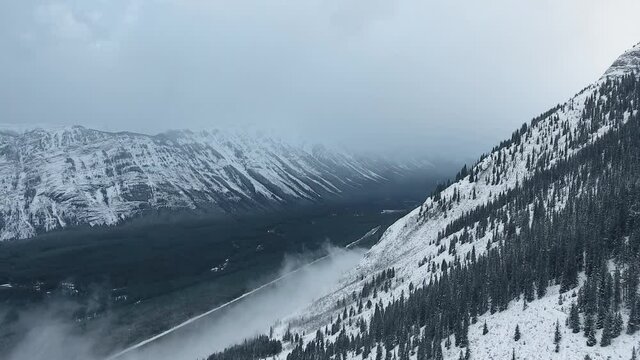 Drone filming winter landscape with mountains covered with black frozen forest in Kananaskis, Alberta, Canada