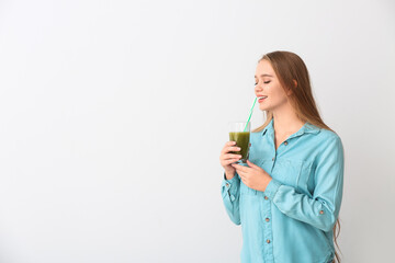 Young woman with wheatgrass juice on light background
