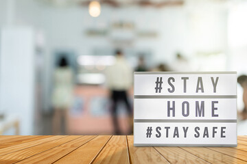 Lightbox sign with text hashtag #STAY HOME and #STAY SAFE with blurred customer, blurred coffee shop background. COVID-19. Stay home save concept.