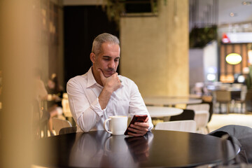 Businessman sitting in coffee shop while thinking and using phone