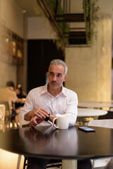 Portrait of handsome businessman sitting at coffee shop while thinking