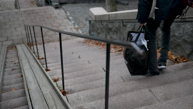 Caucasian male homeless man walking with lots of bags down the stone staircase in a cold city, in slow motion