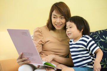 Asian mother is reading a storybook to her son.