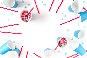 The concept of preparing for a party, event, celebration. Blue paper cups, red straws, snowflakes  and colorful balls are on a white background. Template for christmas, new year. Flat lay. Copy space.