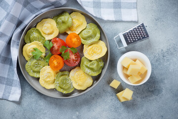 Grey plate with italian ravioli, parmesan cheese and sliced tomatoes, flatlay on a light-blue stone background
