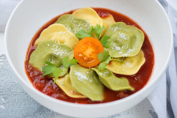 Closeup of a white bowl with italian ravioli served on tomato sauce bedding, studio shot