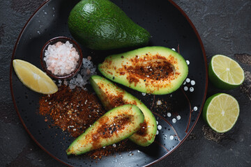 Black plate with avocado, japanese shichimi seasonings, pink salt and lemon, above view, horizontal shot