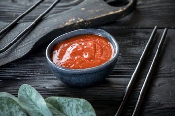 caucasian spicy sauce in a ceramic saucepan. Black wooden background and decor.