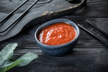 caucasian spicy sauce in a ceramic saucepan. Black wooden background and decor.