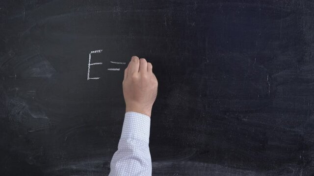 A teacher writes Einstein's formula E=mc2 in chalk on the blackboard