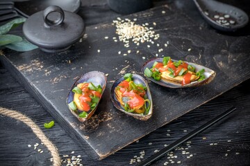 mussels baked on a shell with spicy sauce and green onions. Black background and black decor.