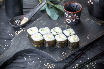 Classic Japanese sushi roll with cucumber and sesame seeds. Black background and black decor.