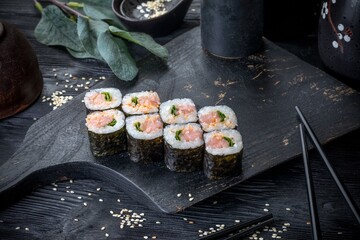 Classic Japanese sushi roll with salmon and green onions. Black background and black decor.