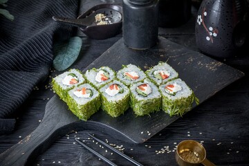 Vegetarian uramaki inside-out roll with cream cheese, green onions, cucumber, bell pepper. Covered with fresh dill. Black background, black decor.