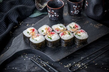 classic sushi roll with mussels, cream cheese, tobiko and green onions. Black background and black decor.