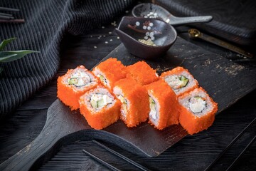 A California roll. Makizushi sushi roll rolled inside-out, and containing cucumber, crab, and avocado. Black background, black decor.