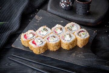 Uramaki roll inside out with eel, tobiko, avocado and cream cheese. Covered with tuna shavings. Black background, black decor.