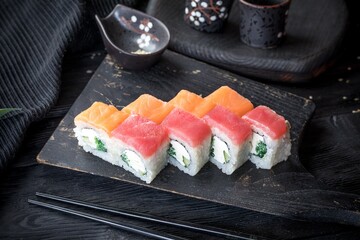Uramaki roll inside out with creamy sauce, fresh cucumber, wakame, tuna fillet and salmon fillet. Black background, black decor.