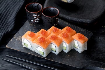 Sushi roll Philadelphia luxe. Japanese rice, salmon, philadelphia cheese, cucubmer, caviar. Black background, black decor.