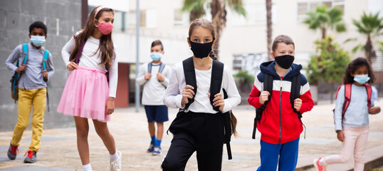 Schoolchildren in masks walking together on the street from school at day