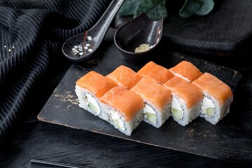 Sushi roll Philadelphia light. Japanese rice, salmon, philadelphia cheese, cucubmer. Black background, black decor.