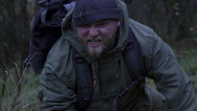 Sad aggressive bearded man with dirty face standing up after falling down in forest.