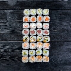 Assorted eight types of sushi rolls on a black wooden background.
