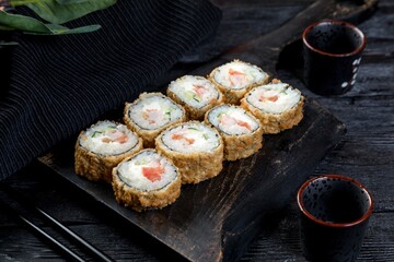 warm tempura sushi roll with shrimps, tomato, cucumber and creamy sauce. black background, black decor.