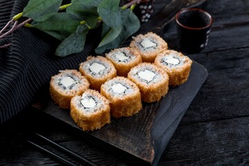 warm tempura sushi roll inside out with creamy sauce. black background, black decor.