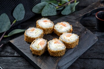 warm tempura sushi roll with lettuce, fish and creamy sauce. black background, black decor.