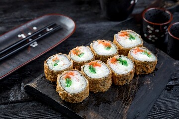 warm tempura sushi roll with crab sticks, capelin roe, wakame and creamy sauce. black background, black decor.