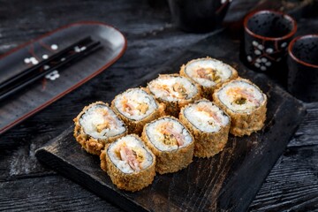 warm tempura sushi roll with seafood. black background, black decor.