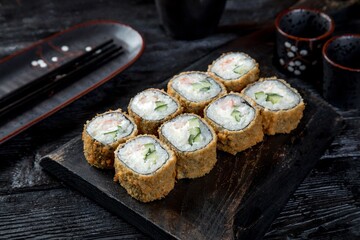 warm tempura sushi roll with shrimp, cucumber and creamy sauce. black background, black decor.