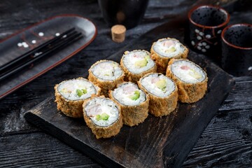 warm tempura sushi roll with avocado, shrimps and creamy sauce. black background, black decor.