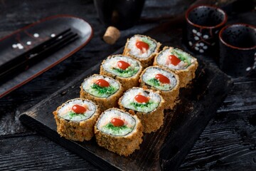 warm tempura sushi roll with wakame, fish fillet, spicy sauce. black background, black decor.