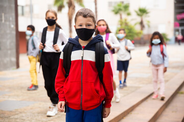 Confident tweenager in protective mask walking with other schoolchildren to school campus after lessons on spring day. Concept of necessary precautions in COVID pandemic