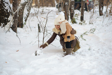 mother and daughter in brown fur coats walk through the winter forest. lots of snow around.