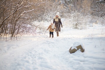 Fototapeta na wymiar mother and daughter in brown fur coats walk through the winter forest. lots of snow around.