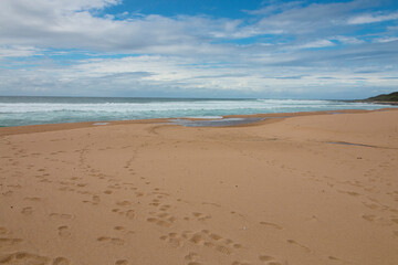 Fototapeta na wymiar Footprints in Sand on Beach Leading Down to Ocean Waves