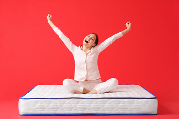 Happy young woman sitting on mattress against color background