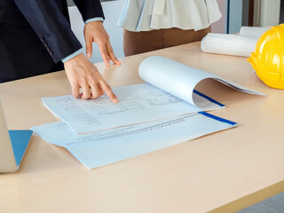 Engineer hand pointing blueprint on wooden desk in the office.